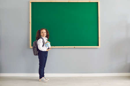 Back to school. Happy schoolgirl is standing smiling on the background of the school blackboard in...