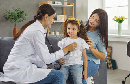 Family doctor visiting her young patient at home. Female pediatrician with stethoscope sitting on...