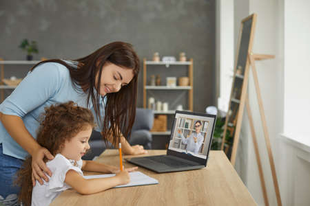 Mum and little child learning at home, sitting at table, watching web tutorial for kids on screen of...