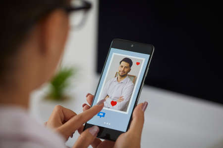 Love, finger of woman pushing heart icon on screen in mobile smartphone application. Online dating app, valentines day concept.の写真素材