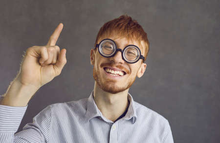 Horizontal shot of bearded amazed handsome guy has excited expression, raises index finger, glad to recieve good idea about improvement his scientific work. Happy pleased male isolated on gray wallの写真素材