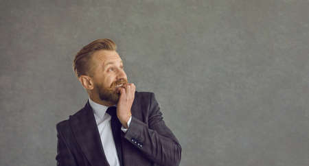 Profile view funny scared bearded young man in suit jacket biting nails and looking to the side at text copy space background. Trouble at work, business problem, making mistake, fear, anxiety conceptの写真素材