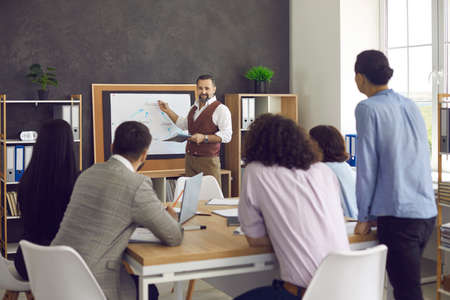 Male leader conducts a morning planning meeting in the office for his subordinates, sets goals,...