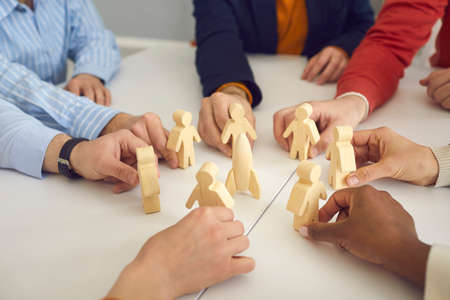 Close up of business team members joining wooden human figures around toy space rocket on office table. Metaphor for teamwork. Symbol of developing group projects and launching new products togetherの写真素材