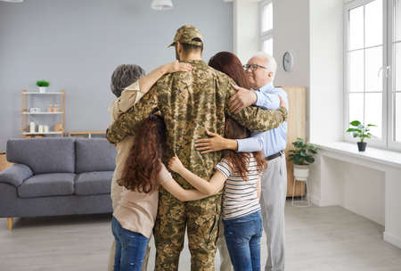 We missed you so much. Family reunited with veteran father whos returned home from military service. Back view portrait happy young soldier in camo uniform standing in living room and hugging familyの写真素材