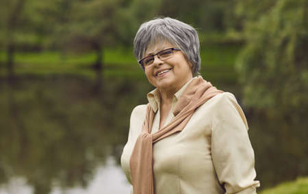 Outdoor portrait of happy senior woman in glasses. Cheerful old lady with short grey hair smiling...