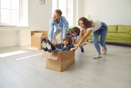 Happy family having fun in new home. Joyful excited first-time buyers with children playing with cardboard boxes in living room interior. Real estate, residential mortgage, buying dream house conceptの写真素材