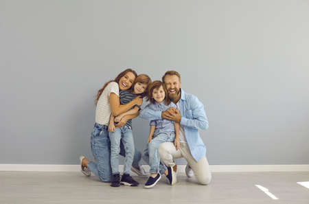 Studio portrait of happy cheerful European family. Loving young mother and father embracing their children. Positive mom, dad and kids in modern casual clothes hugging, smiling and looking at cameraの写真素材