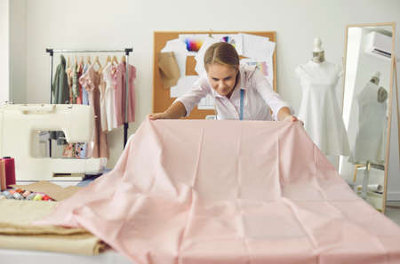 Dressmaker making clothes. Seamstress working in her studio. Tailor looking at new light pink...
