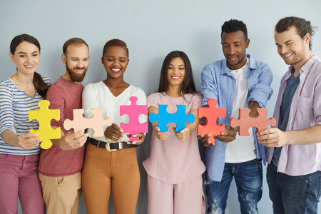 Studio group portrait of six happy smiling multiethnic young people joining big colorful jigsaw puzzle pieces. Team of creative multiracial millennial friends cooperate and find good solution togetherの写真素材