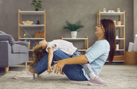 Happy young mother and small preschooler daughter sit on floor in living room play together on weekend. Smiling mom or nanny have fun feel playful with little girl child at home. Motherhood concept.の写真素材