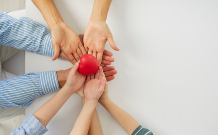 Family holding red heart in hands. Mom, dad and kid feeling united, sharing love, cherishing gift of life, promoting charity, NGO, donation, heart health, healthcare. Top view close up white copyspaceの写真素材