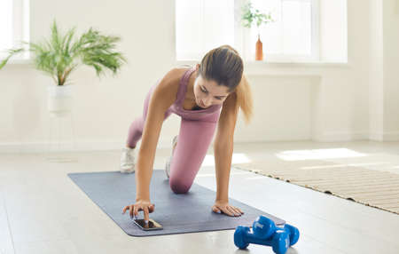 Happy fit young woman who follows steady workout plan is doing sports exercise on fitness floor mat...
