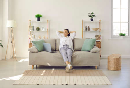 Time to relax. Calm woman with hands behind head sitting on sofa taking break after working with...