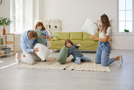 Happy family of four playing, laughing and having fun at home. Cheerful young mom, dad and two children having a pillow fight on the floor in a modern cozy spacious Scandinavian living room interiorの写真素材