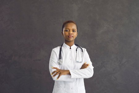 Portrait of serious confident young African American female doctor in white medical uniform on black studio background. Successful millennial ethnic biracial woman nurse or GP. Healthcare, medicine.の写真素材