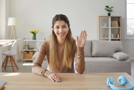 Webcam view of young female blogger waving her hand while recording video or making online call at...
