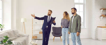 Realtor giving future tenants or first time buyers tour about modern apartment. Boyfriend and girlfriend or husband and wife planning to buy new home and meeting with real estate agent in new houseの写真素材