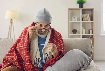 Man who has flu or cold symptoms takes his temperature. Sick middle aged man who has fever is...