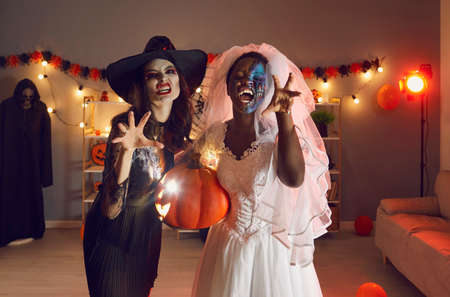 Portrait of two beautiful young women dressed up in spooky Wicked Witch and Dead Bride costumes with...