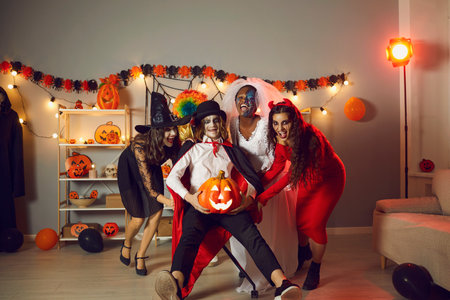 Happy adult people dressed up as evil characters having fun at crazy Halloween horror party at home. Group of girls and their friend in vampire costume fooling around, having fun and laughing togetherの写真素材
