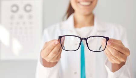 Smiling optician gives you new glasses. Happy doctor in white coat showing modern good quality...