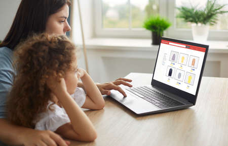 Young ladies enjoying online shopping. Mother and child buying new tops in Internet family clothing store. Happy mom and daughter picking items in fashion outlet with good discounts and free deliveryの写真素材