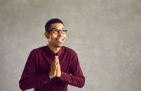 Thankful african american man standing with hands praying looking up studio shot. Face portrait of...