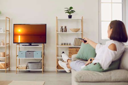 Relaxed woman sitting on couch and watching her favourite TV show. Happy adult lady resting on sofa...
