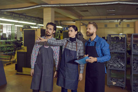 Young woman points finger away at something while giving inspector tour around shoe factory. Workers meeting owner, showing him around footwear making plant and explaining stages of production processの写真素材