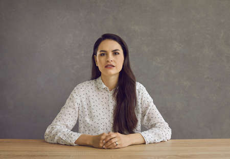 Portrait of a woman sitting at the desk. An attractive woman with black hair in a white blouse sits...