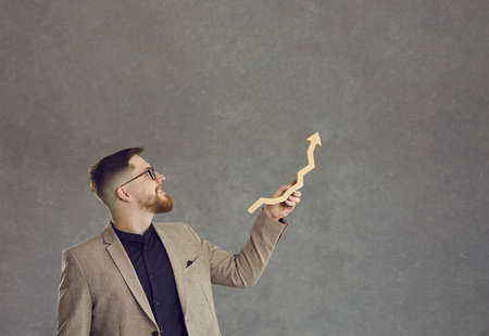 Good manager makes investment growth. Happy successful businessman holds a growth arrow and shows it up standing on a gray background. Business concept of growth, success and achievement.の写真素材