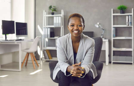 Portrait of smiling young African American woman sit in chair in office look at camera show leadership. Happy millennial ethnic businesswoman speak talk on video webcam online call. Diversity concept.の写真素材