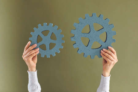 Human hands connecting two gear wheels. Cropped shot of anonymous woman holding up 2 green...