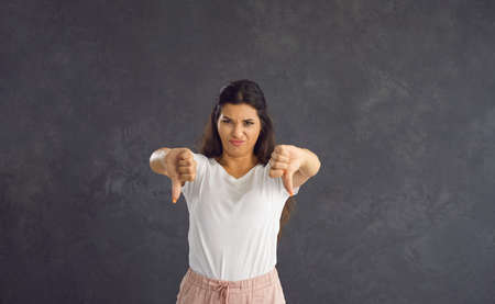 Portrait of unhappy young Caucasian woman isolated on black background show thumb down dislike bad...