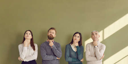 Group of thinking people trying to answer hard question. Four people with pensive face expressions standing in row with hands on chins and looking up at green text copyspace for thought bubbles aboveの写真素材