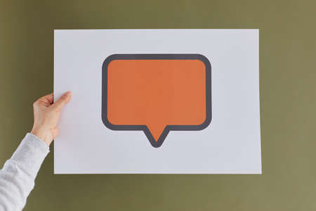 Anonymous adult woman showing one orange mock up copyspace speech balloon or message bubble on green background. Female hand holding paper with free, blank, clean mockup space for expressing opinionの写真素材