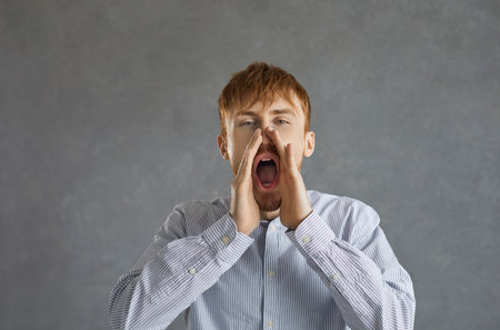 Photo of a screaming man with palms on his face and open mouth, staring directly at a gray...