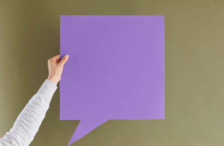 Express your thoughts. Unknown woman holding blank purple paper card in form of speech bubble on green khaki background. Concept of important messages, thoughts and ideas. Copy space.の写真素材