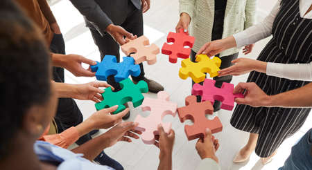 Banner background with multiracial team of adult business men and women connecting red, pink, yellow, blue and green pieces of jigsaw puzzle. Concept of teamwork, innovative solutions, creative ideasの写真素材
