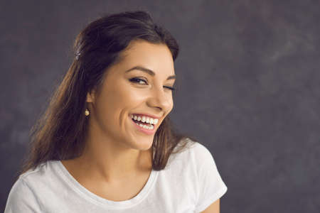 Close up portrait of smiling millennial Latino woman on black studio background eye wink look at camera. Happy young Hispanic girl laugh show positive optimistic face expression. Body language.の写真素材