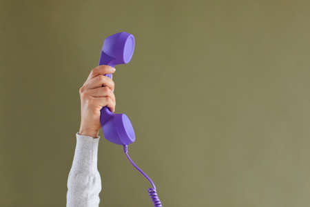 Close up of person hold handset isolated on green studio background for communication or conversation. Landline telephone call for customer service support. Feedback and helpline concept.の写真素材