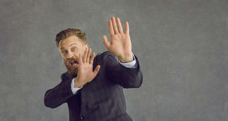 Caucasian middle-aged businessman with emotion of panic and fear on a gray background. Frightened man shouts and shows a stop sign. Concept of human emotions and facial expression.の写真素材