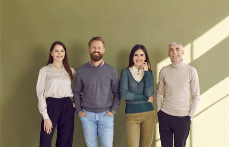 Group portrait of four happy people in smart casual outfits posing against green studio background....