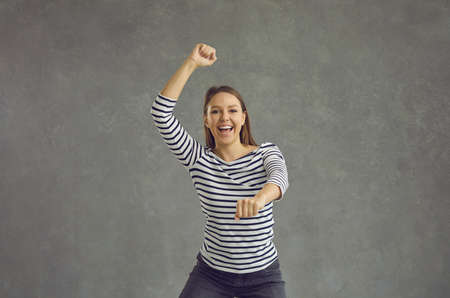 Delighted young woman dances carefree on a gray background celebrating victory and success. Cheerful...