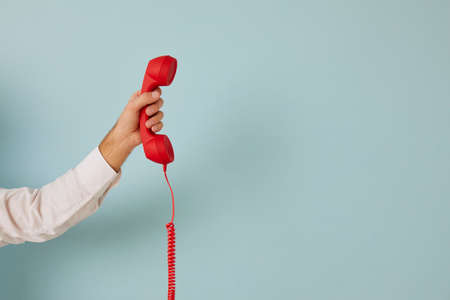 Unidentified man holding red wired retro telephone handset on light blue banner background. Male...