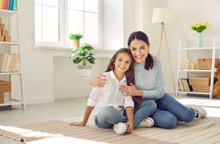 Portrait of smiling young Caucasian mother and small teen daughter sit hug at home show love and...