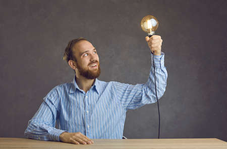 Portrait of excited man freelancer or entrepreneur holding glowing bulb in hand looking at light...