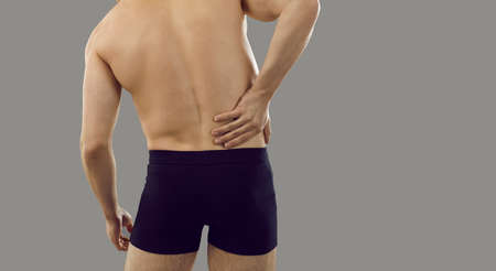 Backside of man suffering from pain in his right side. Rear view from behind of young patient in...