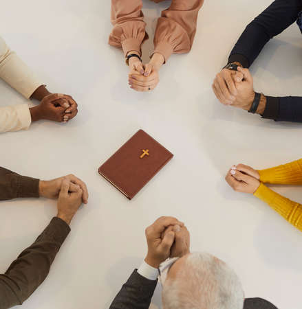 Diverse group of different religious multiracial multiethnic people praying to God together. Cropped shot of human hands on table around the Holy Bible. Religion, christianity and discipleship conceptの写真素材